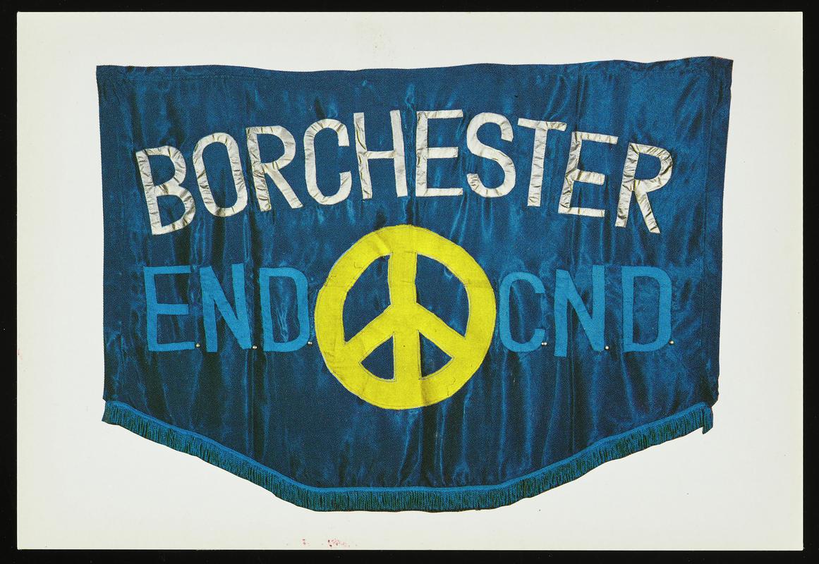Colour postcard of a Borchester End CND banner. Original banner Designed and made by Thalia Campbell and Jan Higgs for the recording of the Archers Christmas Concert at Crosby on October 22nd, 1982.