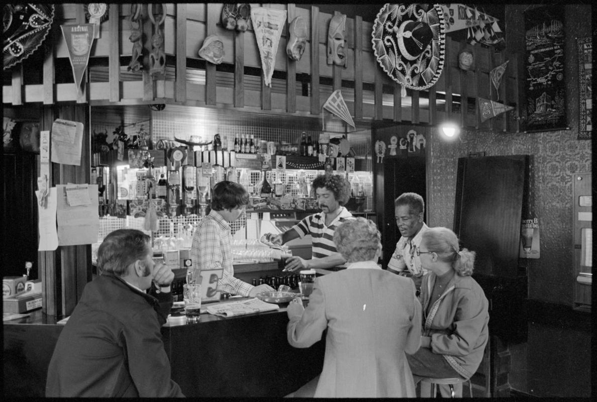 Interior view of the Ship & Pilot public house showing people drinking at the bar, Mount Stuart Square, Butetown.