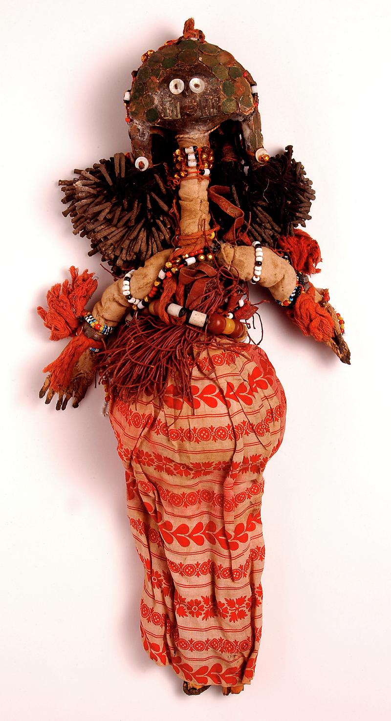 Fertility doll, silk by witches to childless woman in the Sudan ; grotesque and characteristic shape, and covered with charms and amulets of many colours; doll is of human shape with long bamboo neck covered with cotton, bamboo legs and an undetermined he