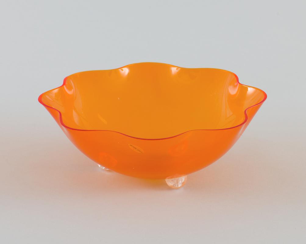 Orange plastic fluted edge fruit bowl with three clear plastic semicircle 'legs'.