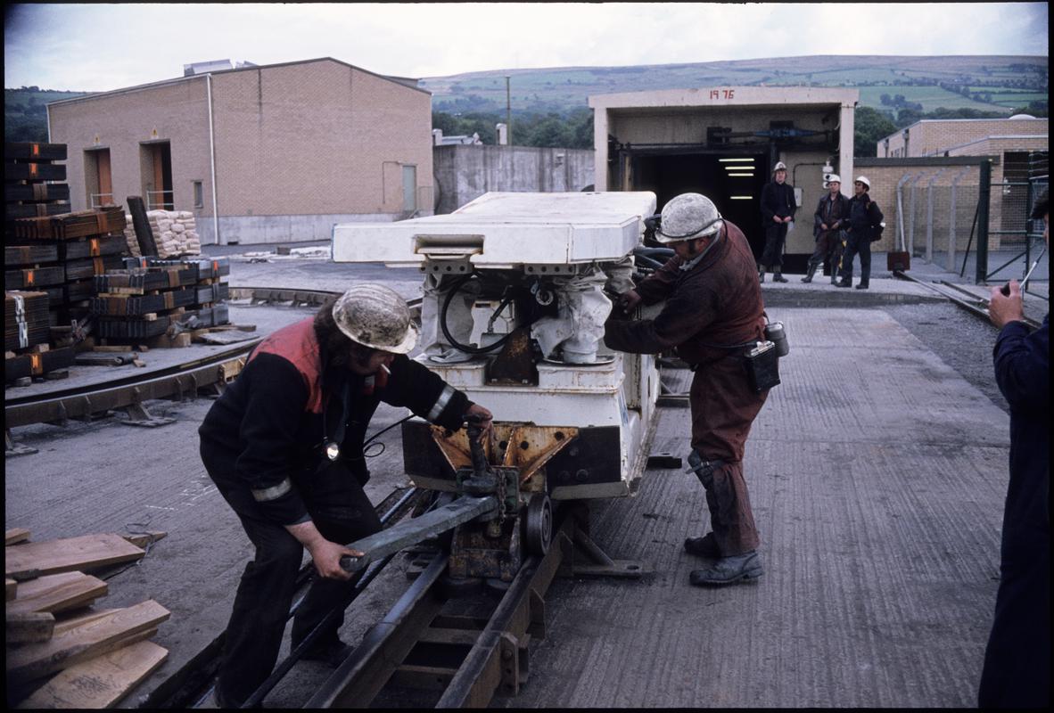 Colour film slide showing men loading a powered support onto a Becorit floor base mono rail. Betws Mine September 1979.