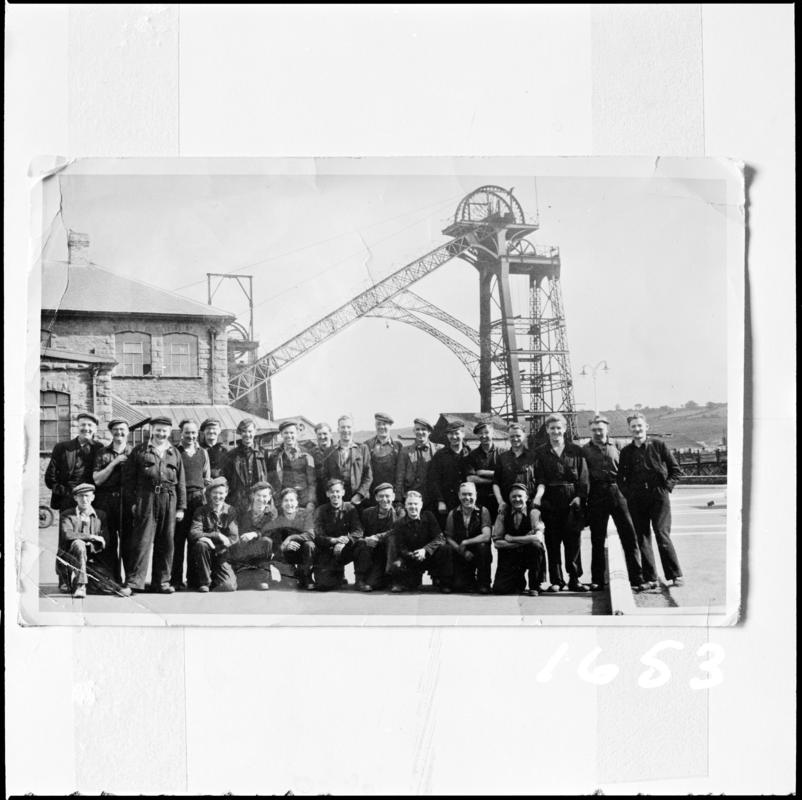 Black and white film negative of a photograph showing a group of miners stood in front of the headgear, Deep Navigation Colliery.