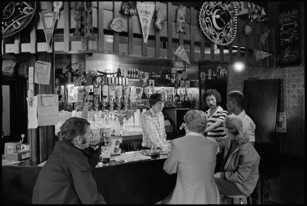 Interior view of the Ship & Pilot public house showing people drinking at the bar, Mount Stuart Square, Butetown.