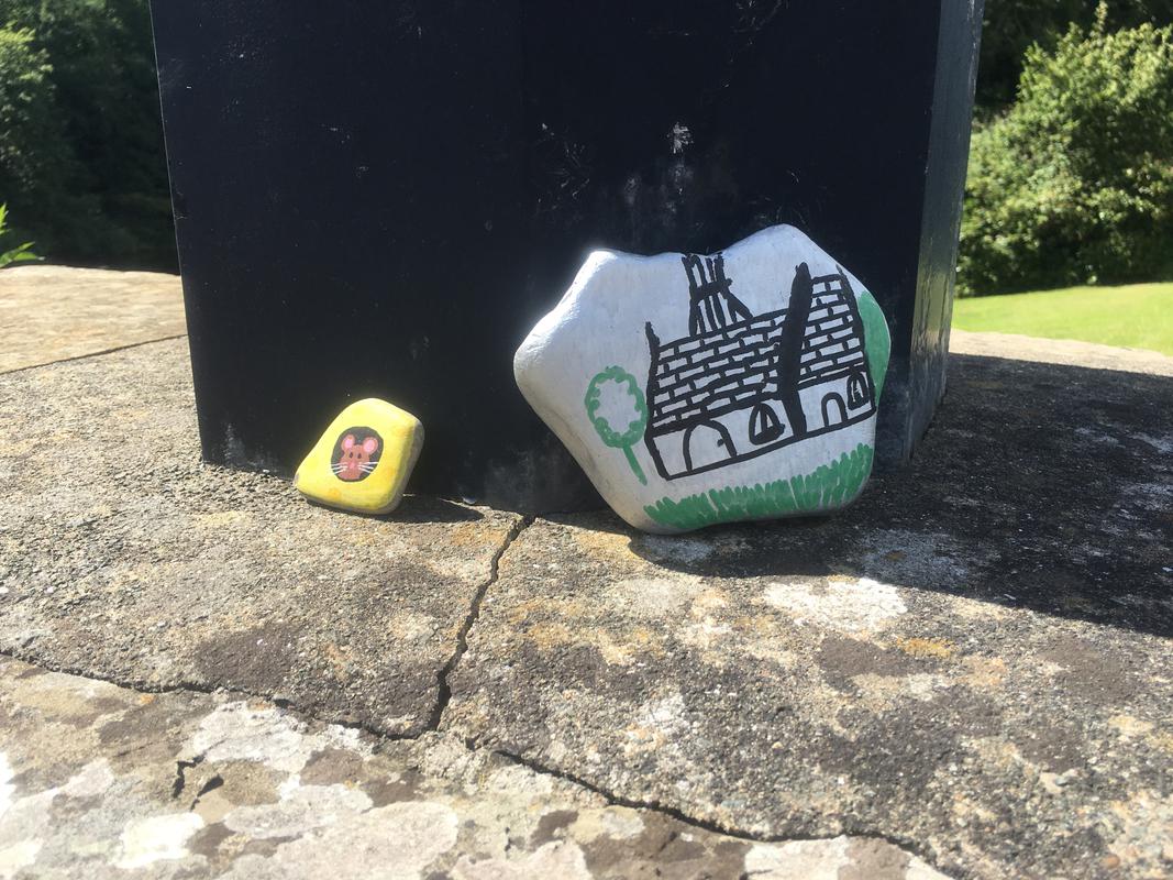 A pebble painted to depict a piece of cheese with a hole with a mouse looking out and another pebble depicting a painting of Boughrood Church. On Boughrood Bridge, over the River Wye, Boughrood, Powys.