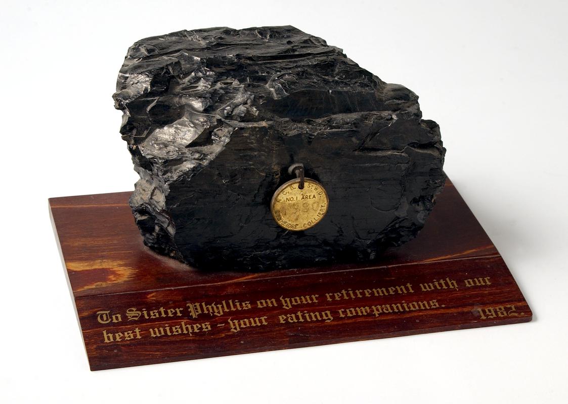 Lump of coal on wooden plinth with inscription in gold.