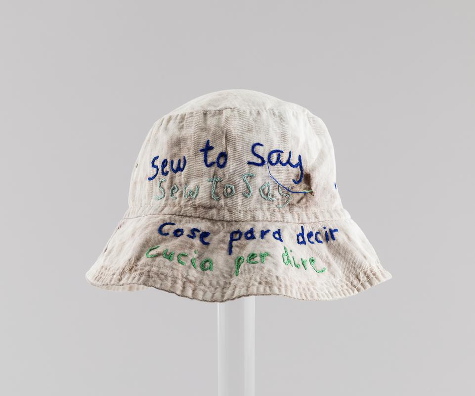 White hat with blue and green embroidery. Worn by Thalia Campbell in 1995 on the 'WILPF 'Women's International League for Peace and Freedom 'Sew to Say' march from Helsinki to Beijing.