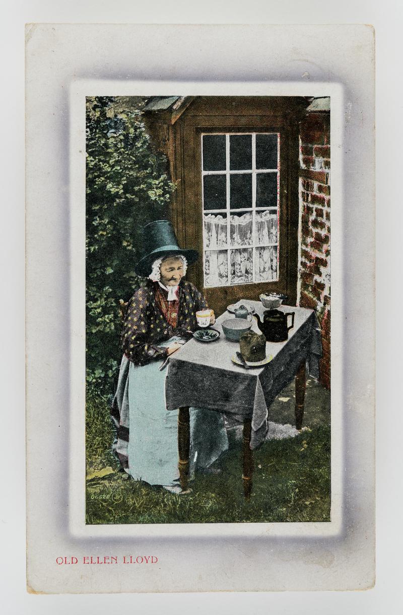 Old Ellen Lloyd, Bettws-y-coed, seated at tea table outside her house, wearing Welsh costume.