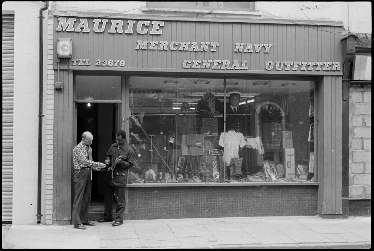 Exterior view of 'Maurice Merchant Navy General Outfitter', 5 James Street, Butetown, showing the proprietor Mr M. Colpstein assisting a customer.