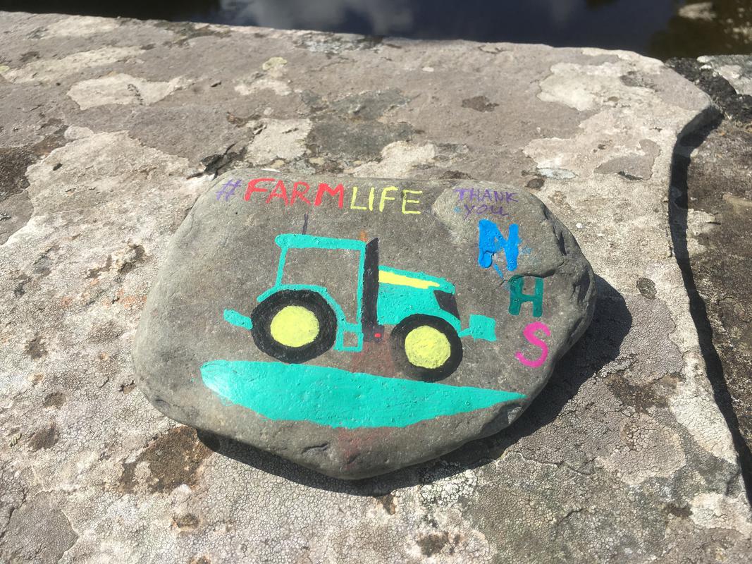 A pebble depicting a painting of a tractor and the words reading '#Farmlife Thank you NHS' on Boughrood Bridge, over the River Wye, Boughrood, Powys.