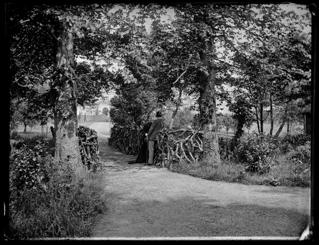 Gardens of Pencisely House, Pencisely Road, Cardiff, showing a man and woman stood (possibly Walter Insole and his wife) on a rustic bridge.