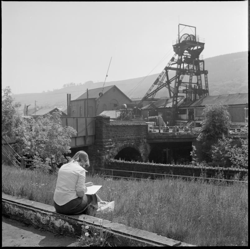 Black and white film negative showing a woman sketching a surface view of Deep Duffryn Colliery 1977.  'Deep Duffryn 1977' is transcribed from original negative bag.