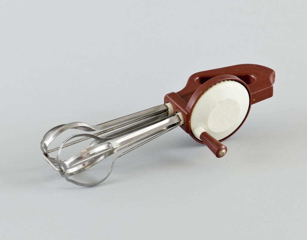 Stainless steel rotary whisk with plastic brown and cream handle, with makers name embossed on cream disk.