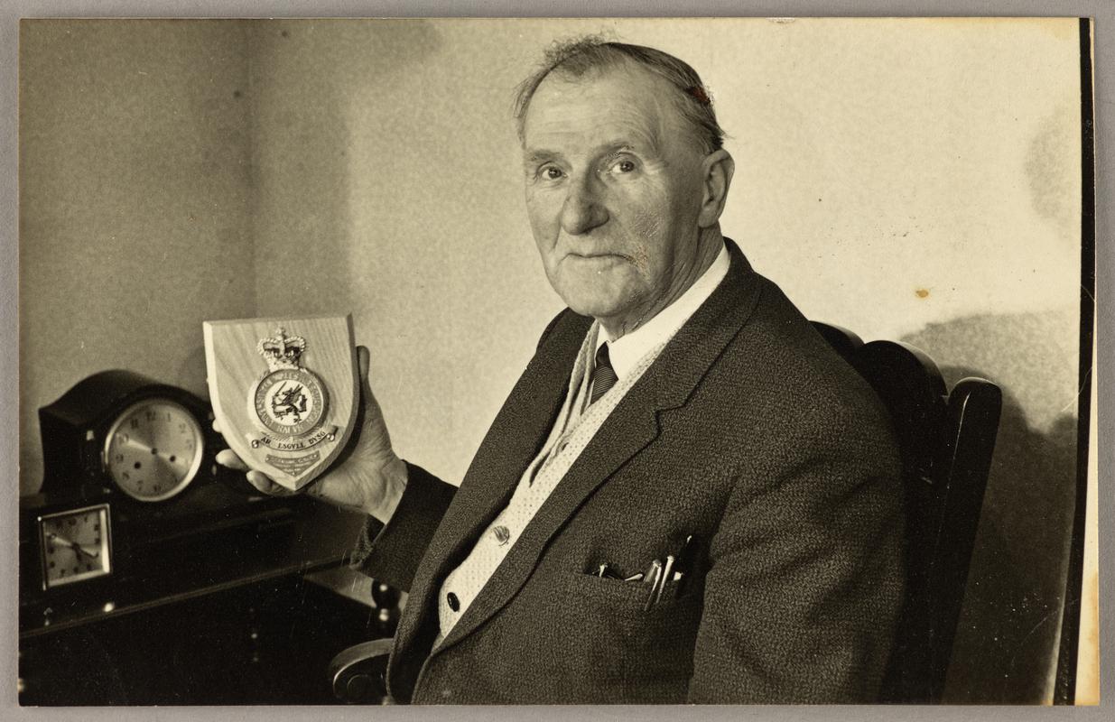 View of C.H. Watkins sitting in chair holding trophy.
