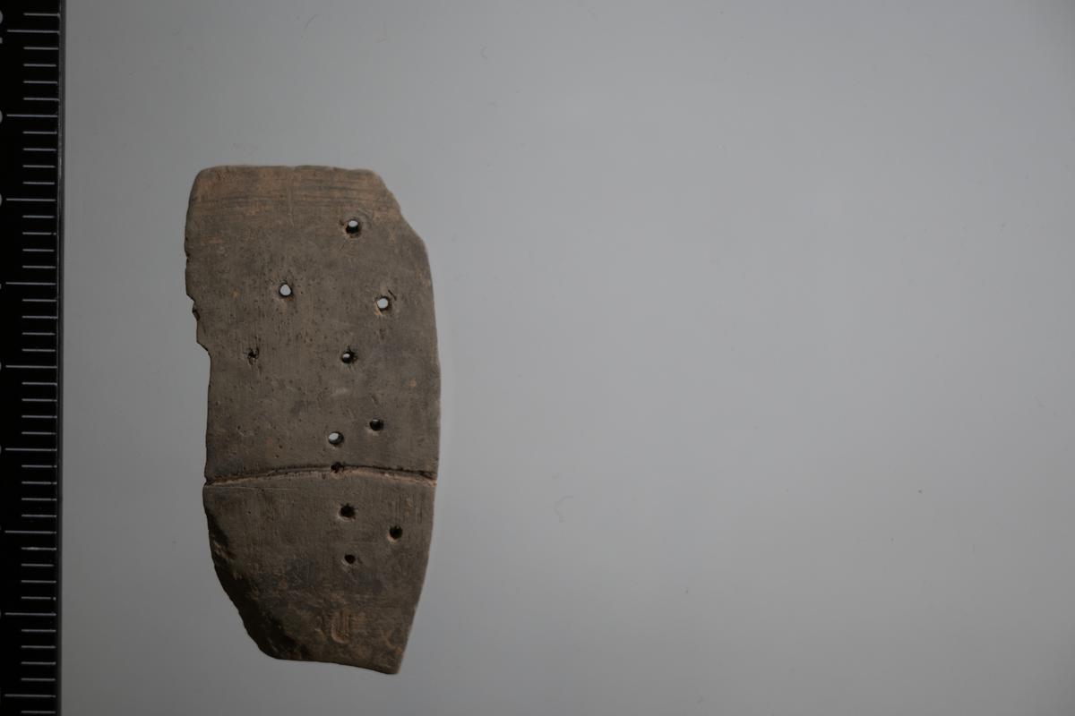 Greyware strainer with perforations and incised line decoration.