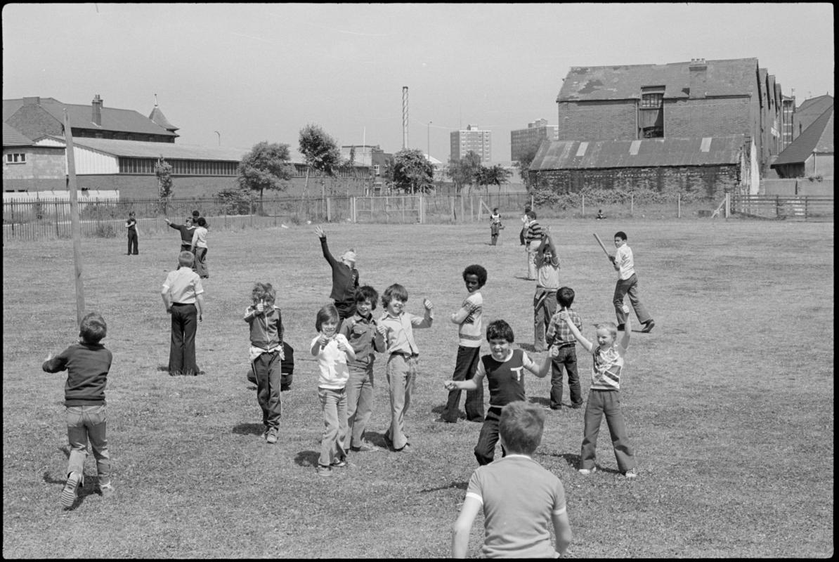 Children playing in the large grass playground surrounding Mountstuart Primary School, Adelaide Street, Butetown.