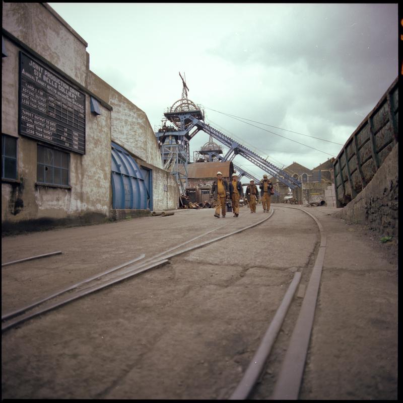 Colour film negative showing miners at the end of their shift walking away from pit top, Six Bells Colliery.  'Six Bells' is transcribed from original negative bag.