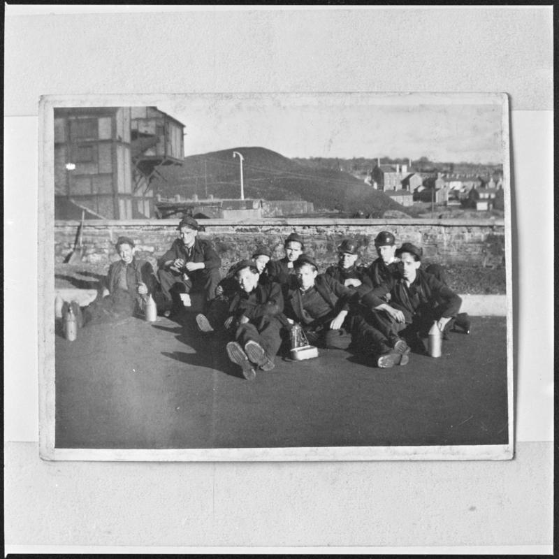 Black and white film negative of a photograph showing a group of miners sat on the ground, Deep Navigation Colliery.  'Deep Navigation' is transcribed from original negative bag.