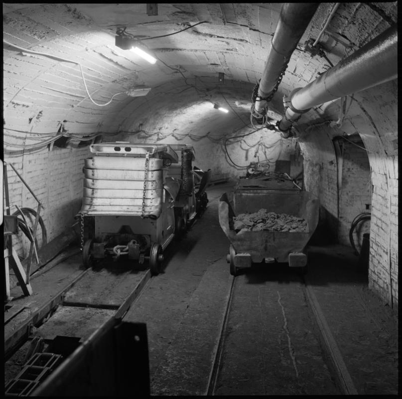 Black and white film negative showing hydraulic roof supports and drams, pit bottom, Nantgarw Colliery.