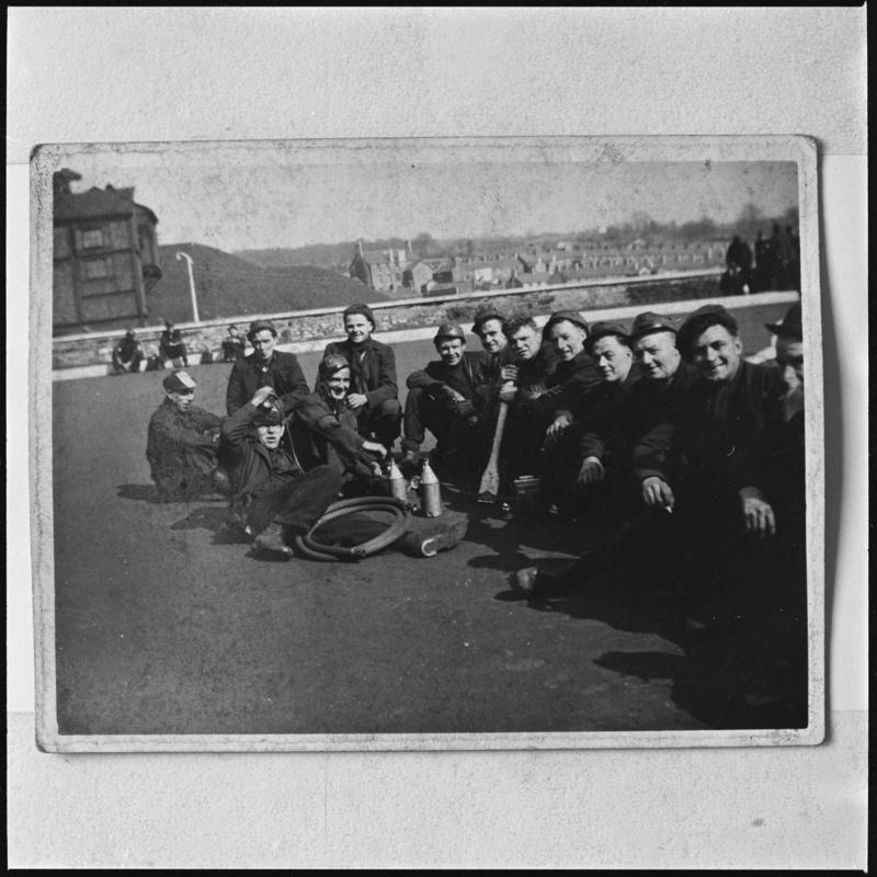 Black and white film negative of a photograph showing a group of miners sat on the ground at Deep Navigation Colliery.  'Deep Navigation' is transcribed from original negative bag.