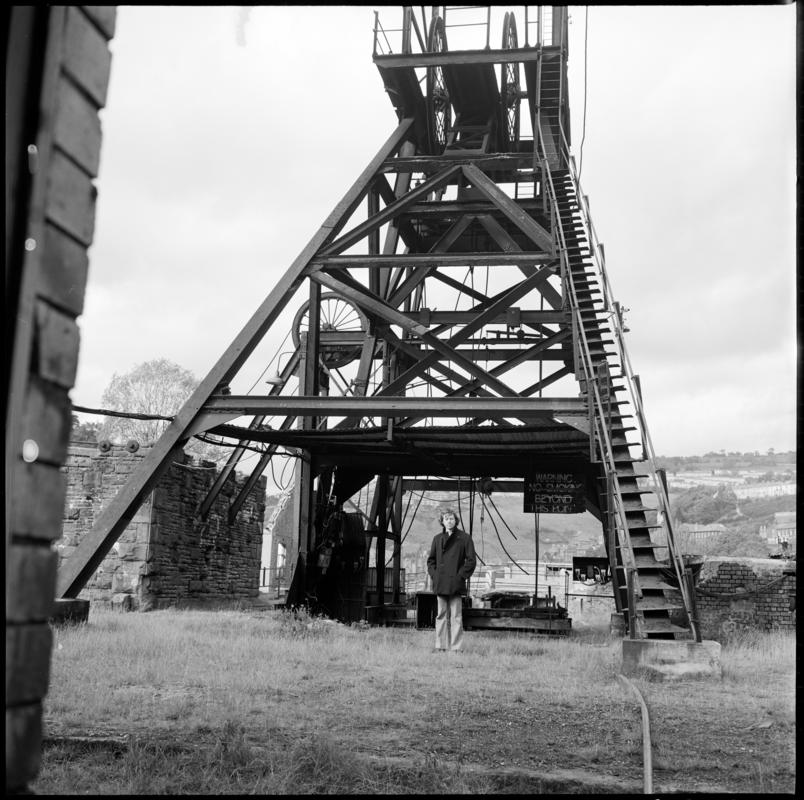 Black and white film negative showing a man stood at the base of the headframe,  Llanhilleth Colliery.  'Llanhilleth' is transcribed from original negative bag.