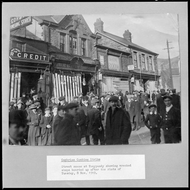Black and white film negative of a photograph showing a street scene at Tonypandy.  Shops are boarded up after the riots of Tuesday 8 November 1910 (information taken from caption below the photograph).  'Cambrian Strike 1910' is transcribed from original negative bag.