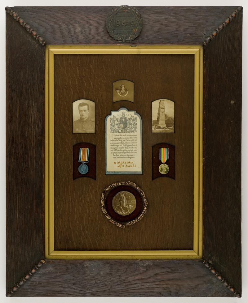 Framed photographs, medals, a bugle and a certificate commemorating Lance-Corporal John Short of the Oxfordshire and Buckinghamshire Light Infantry. Top of the frame features a carved inscription '1914 - 1919' within a wreath.