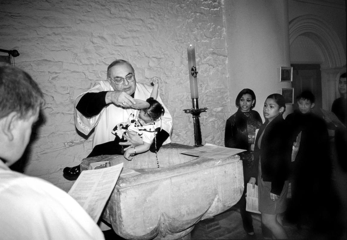 GB. WALES. Cardiff. Butetown - once know as 'Tiger Bay'. Father Jordon baptising a local child at St Mary's Church, Bute Street. 1999