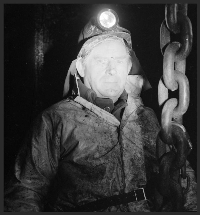 Black and white film negative showing a shaftsman inspecting the shaft from the roof of the cage, Deep Duffryn Colliery, 29 November 1979.