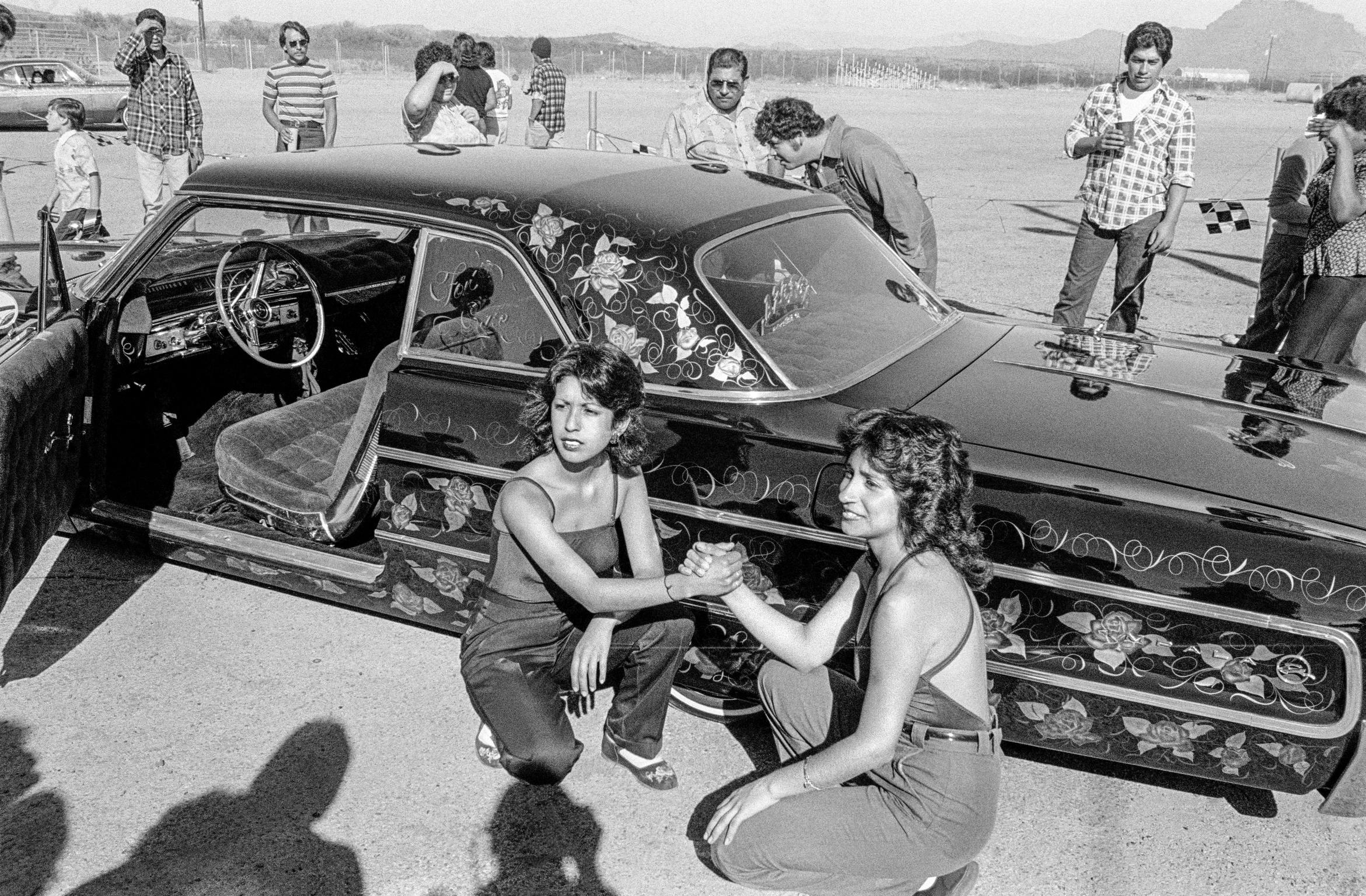 Two girl friends pose for their photograph, in front of a prize winning car, at a Low Riders meeting on the outskirts of Phoenix. Arizona USA