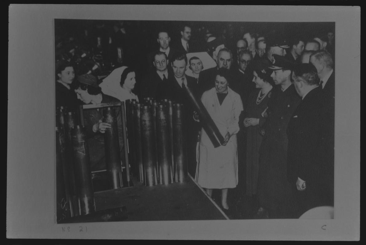 Film negative of a photograph showing visit of King George VI and Queen Elizabeth to Currans, Butetown during World War II. King and Queen inspecting shell held by worker.