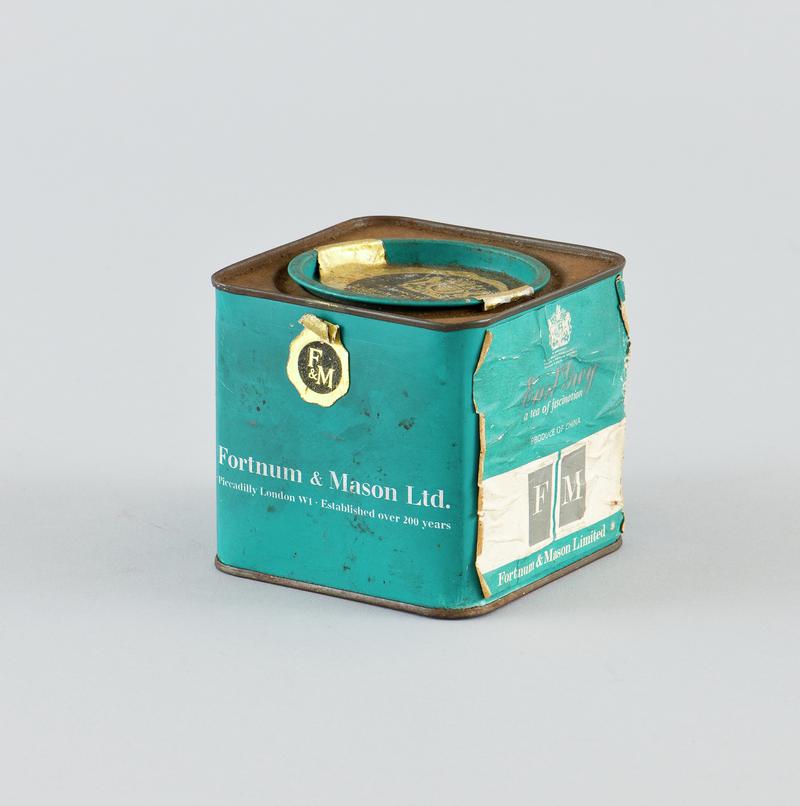 Square tin with teal and white paper label attached around body, with teal circluar lid at center of the top which has paper royal warrant label. That once contained Fortnum & Mason loose Early Grey tea.