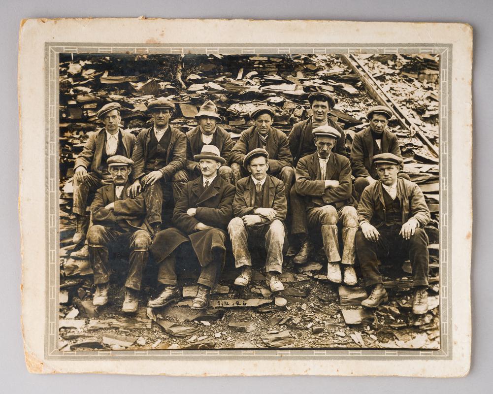 Group photograph of 11 Penrhyn quarry workers. Date '1.4.26' painted on slate in front of workers.