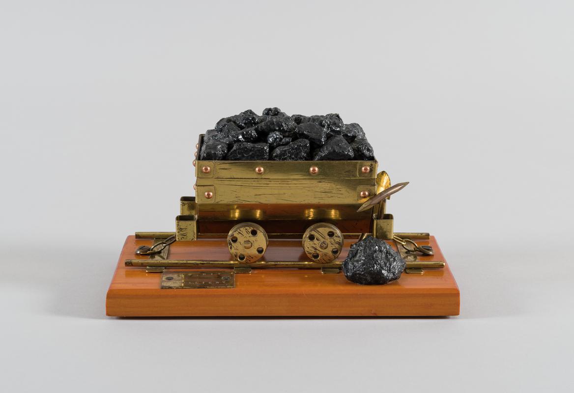Model coal dram in brass on a wooden plinth.