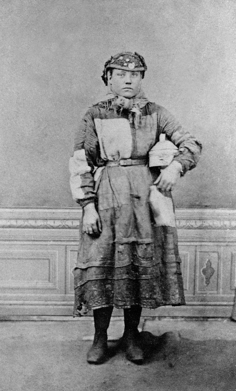 Girl employed on surface at a colliery or an ironworks, holding a food tin and 'water jack'.