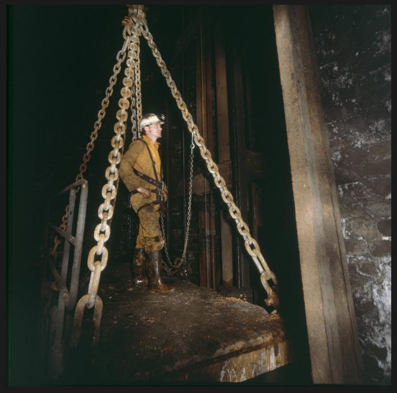 Colour film slide showing Dick, one of the Ty Mawr Colliery shaftsmen, carrying out a routine inspection of the Hetty Shaft from the roof of the cage, 30 June 1983.
