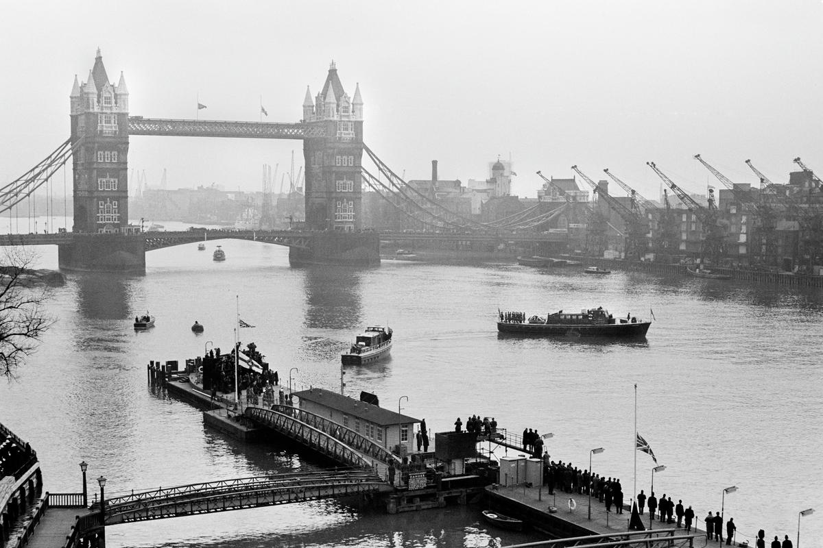 GB. ENGLAND. London. Winston CHURCHILL funeral. 3 January. As Churchill's lead-lined coffin passed up the River Thames from Tower Pier to Festival Pier on the MV Havengore dockers lowered their crane jibs in a salute. 1965.