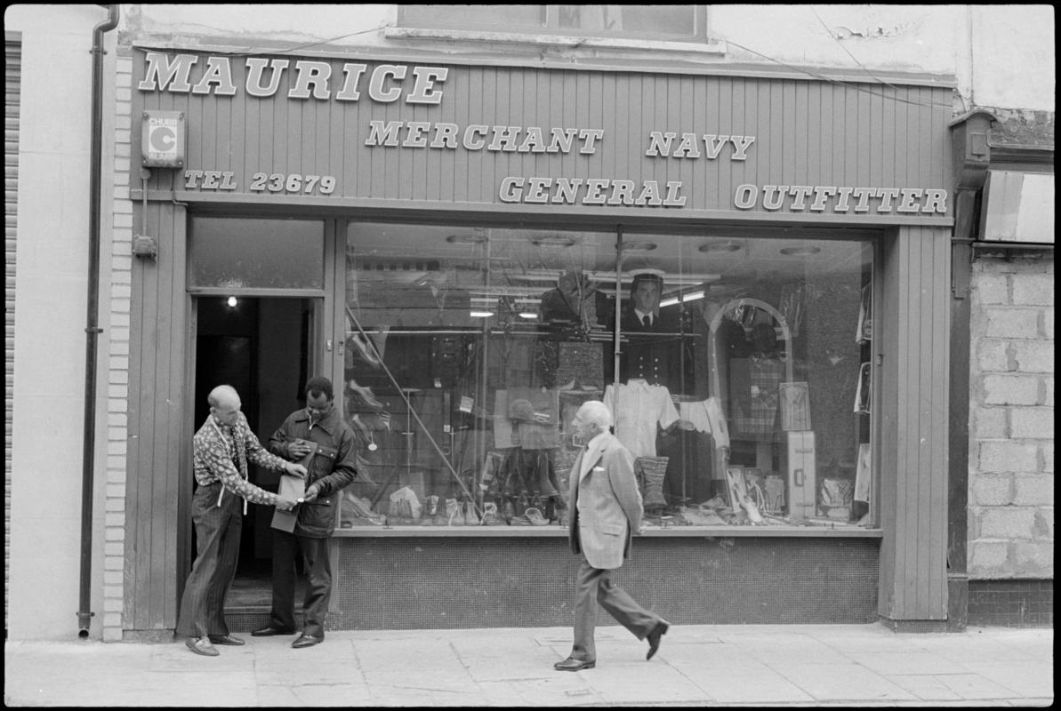 Exterior view of 'Maurice Merchant Navy General Outfitter', 5 James Street, Butetown, showing the proprietor Mr M. Colpstein assisting a customer.