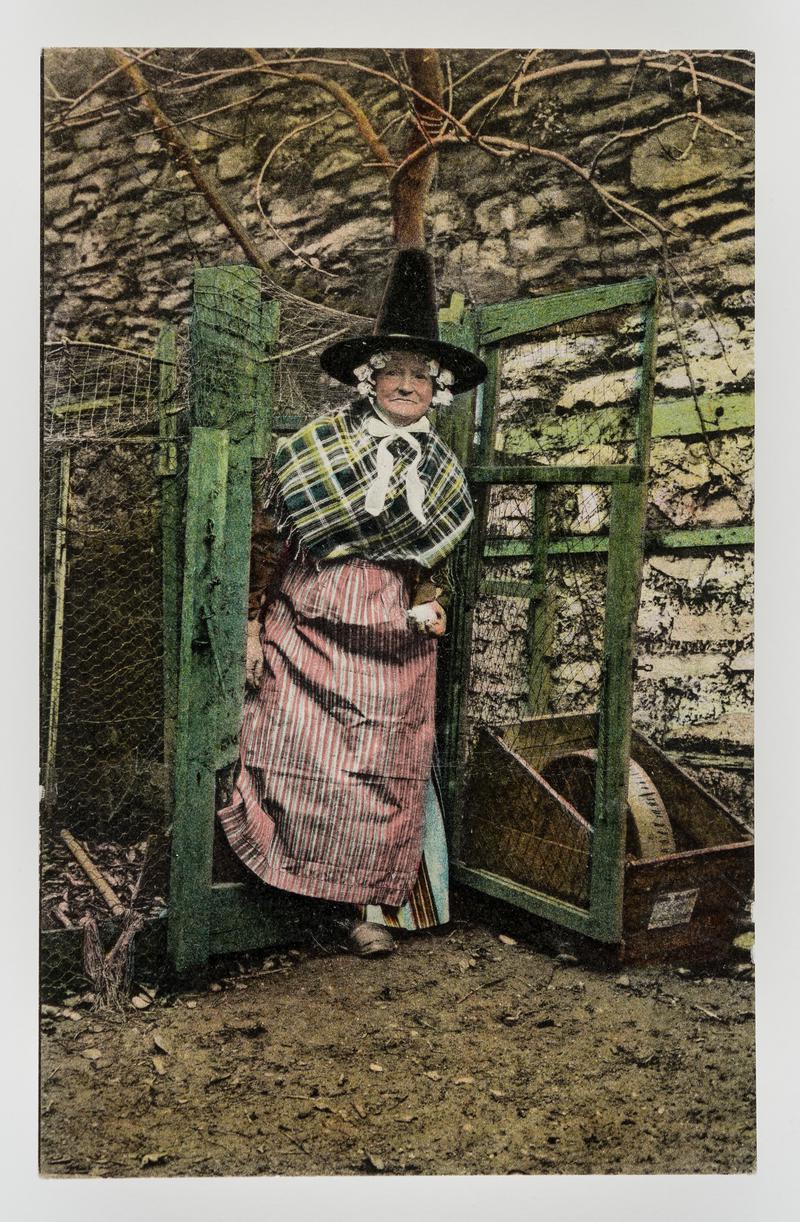 Woman in Welsh costume stepping through gate in fence.