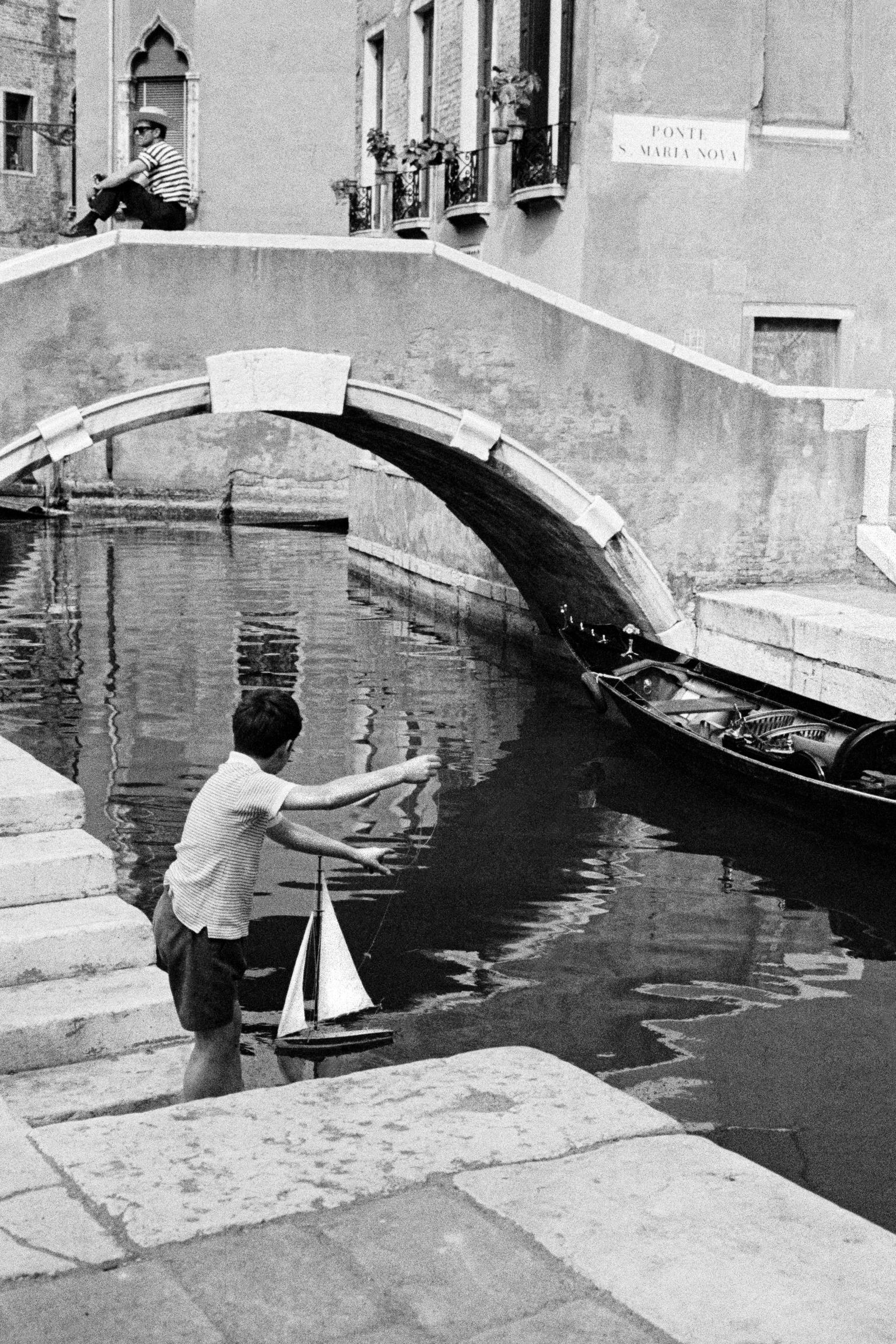 Child playing with his model yacht in one of the canals of Venice. Venice. Italy