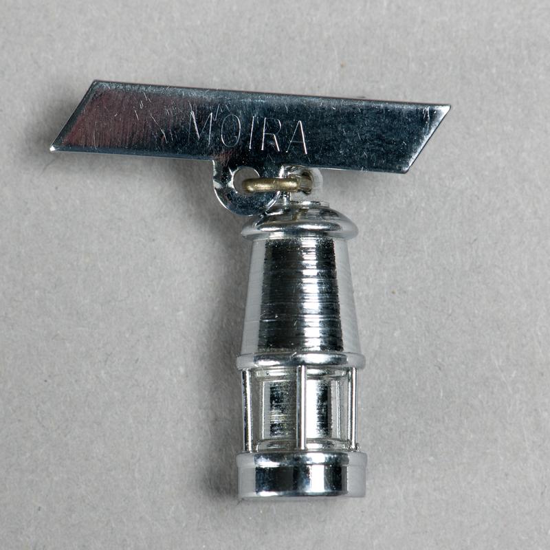 Brooch consisting of a miniature miners lamp attached to a bar inscribed 'MOIRA'.