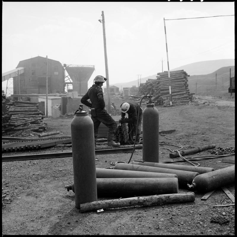 Black and white film negative showing two men working at the Blaenavon drift yard.  The washery is in the background.