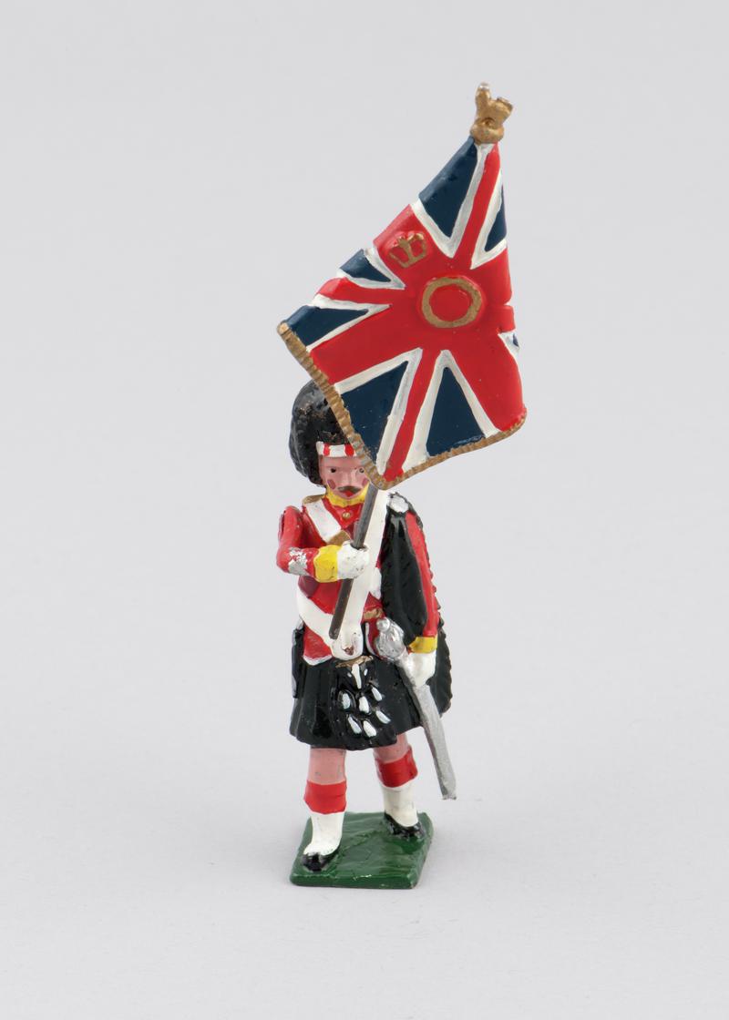 Model of an Argyll & Sutherland Highlander holding regimental colours (Union Jack), 1914. Left arm holds removable flag. Arm is movable. Hand-painted.