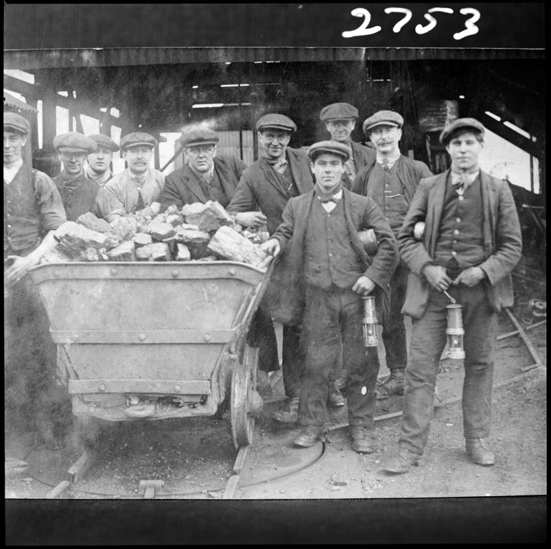 Black and white film negative of a photograph showing a group of miners gathered around a coal dram. 'Men with Tram' is transcribed from original negative bag.