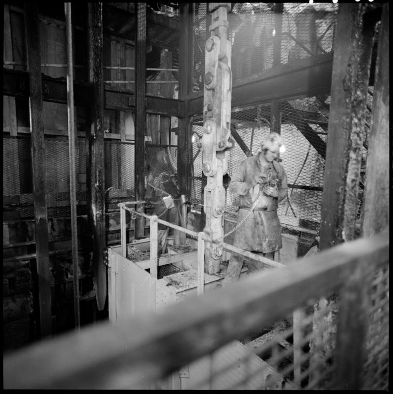 Black and white film negative showing man carrying out maintenance work, near the skip at pit bottom, Lady Windsor Colliery.
