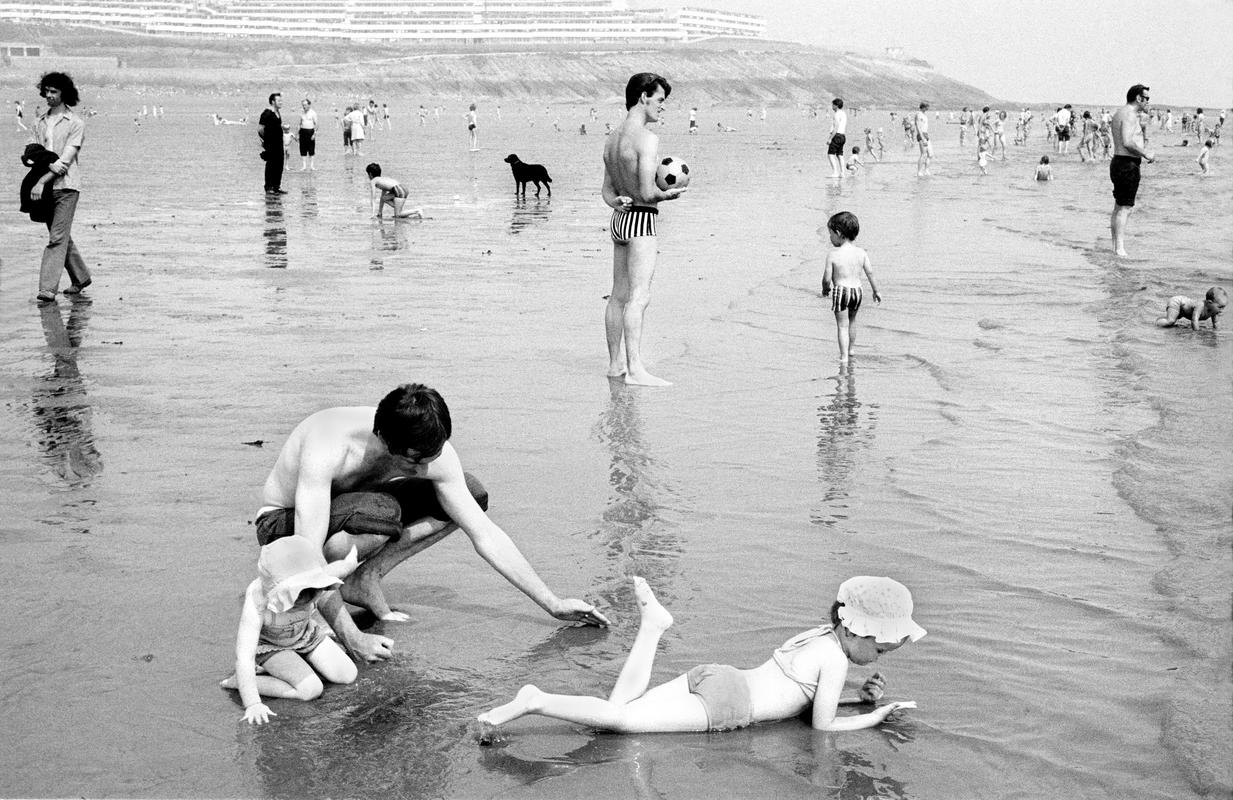 GB. WALES. Barry Island. General. A father with his children relax on the beach at Barry Island, South Wales.  The picture is during the 'miners' week' the holiday period of the miners of South Wales.  It is probable that most of the people on the beach are miners on their holiday.  Due to the closing of the pits this cultural happening no longer takes place. 1973