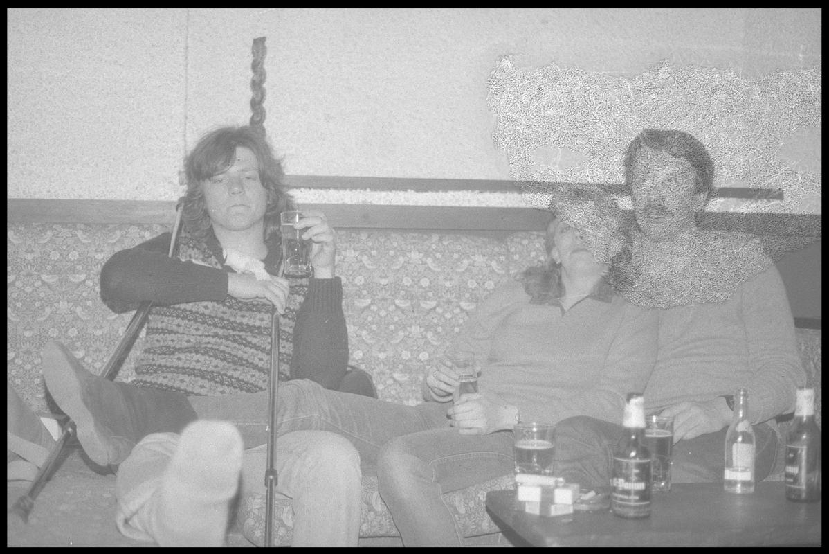 Three unidentified people sitting at table, outdoors. Possibly members of the TNT Group. Location unknown.