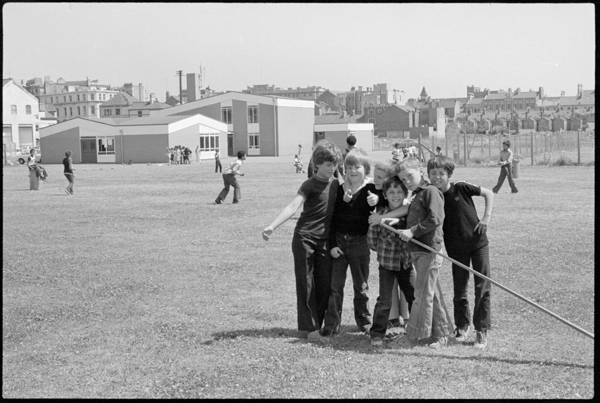 Children playing in the large grass playground surrounding Mountstuart Primary School, Adelaide Street, Butetown. School visible in the background.