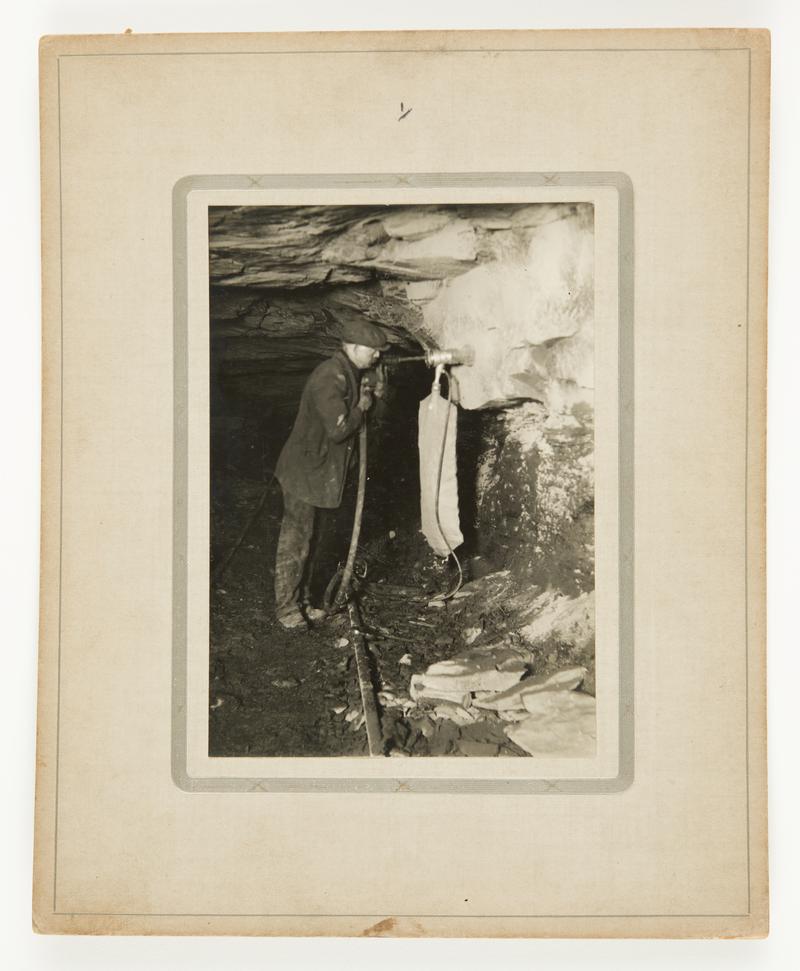 Photograph showing Stan Williams' dust trap invention in action underground. Mounted on card.