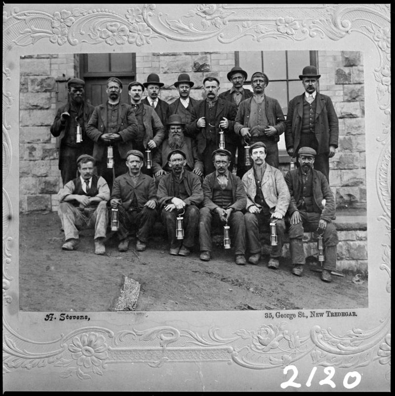 Black and white film negative of a photograph showing a group of New Tredegar miners.  Caption on photograph reads '35 George St, New Tredegar'.  'Tredegar Miners' is transcribed from original negative bag.