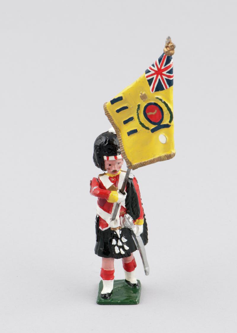 Model of an Argyll & Sutherland Highlander holding regimental colours (yellow), 1914. Left arm holds removable flag. Arm is movable. Hand-painted.